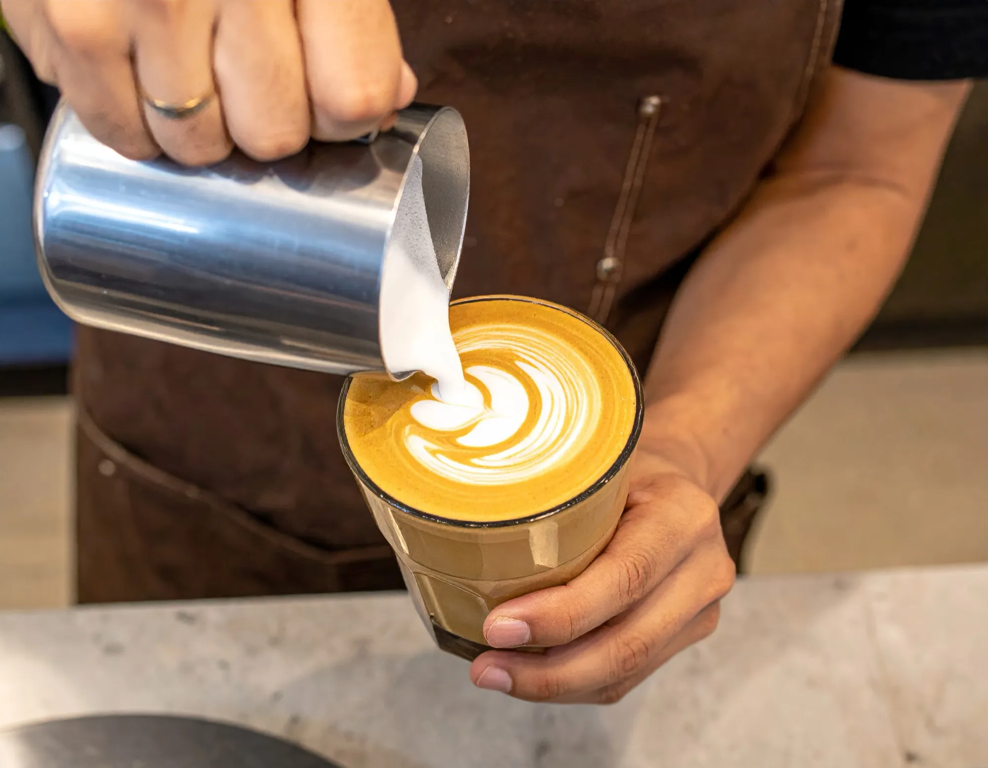 Barista in Schürze gießt Milchschaum zu Latte Art